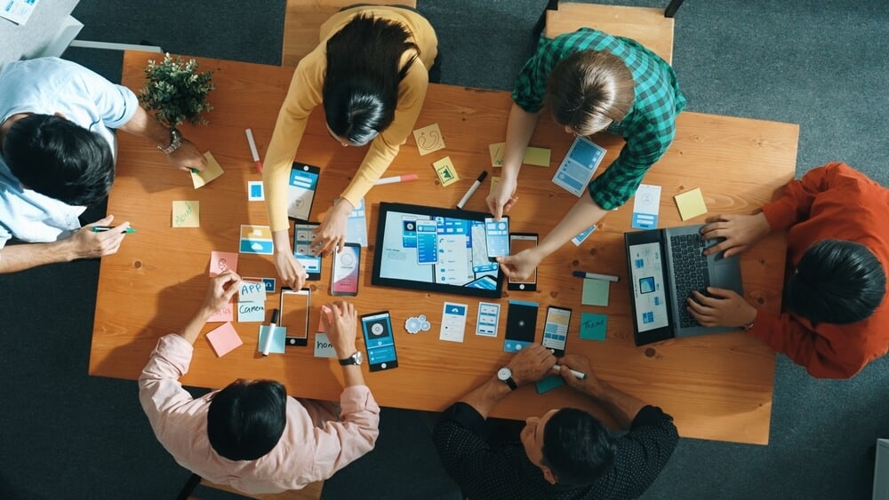 A group of people surrounding a table coming up with ideas for a product that will resonate with consumers.