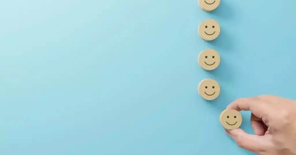 Hand choosing a smiley-face icon from a row, illustrating consumer satisfaction shaped by celebrity marketing.