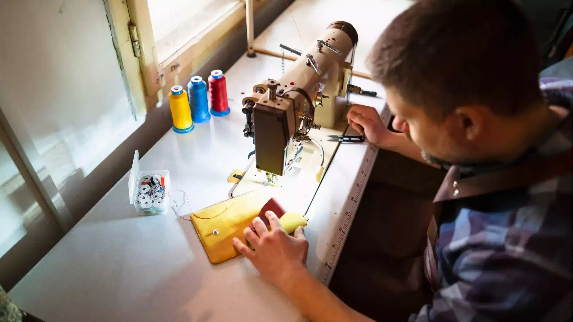 Craftsman sewing a leather item using an industrial machine, demonstrating hands-on unique product development and product innovation in handmade manufacturing