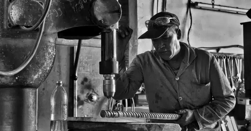 industrial product manufacturing process with machinist operating drill press in workshop