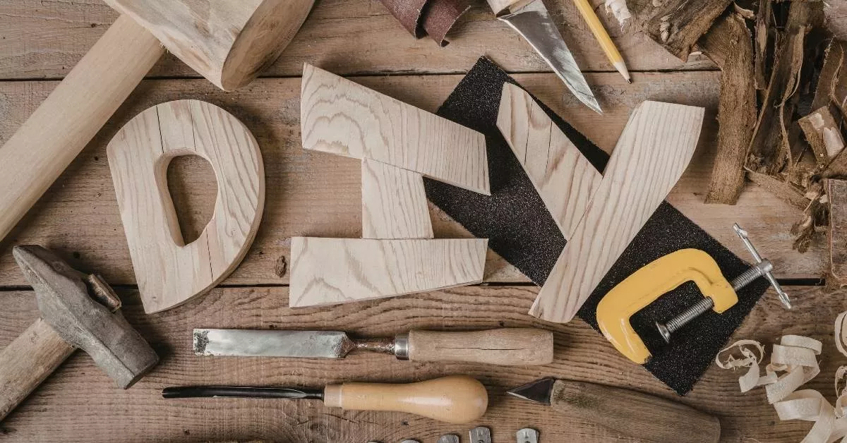 A flat lay of wooden letters spelling DIY surrounded by hand tools, sandpaper, and wood pieces, like a home workshop setup