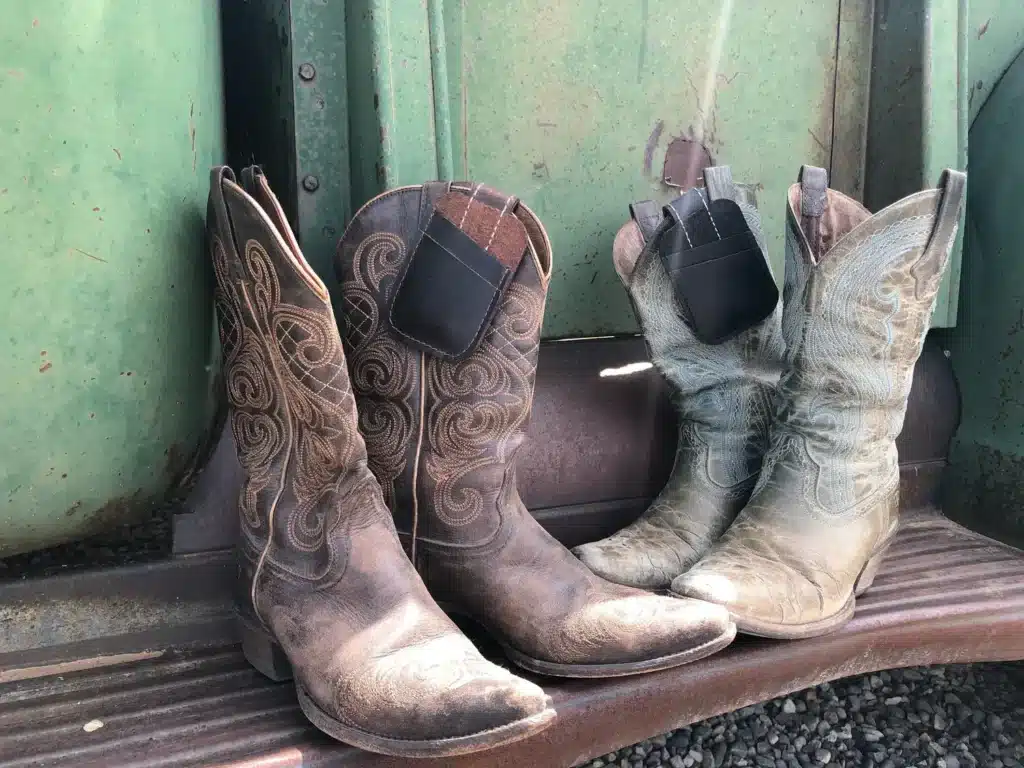 Two pairs of cowboy boots in a truck bed, each with a black leather Boot Pocket wallet clipped inside the boot shaft