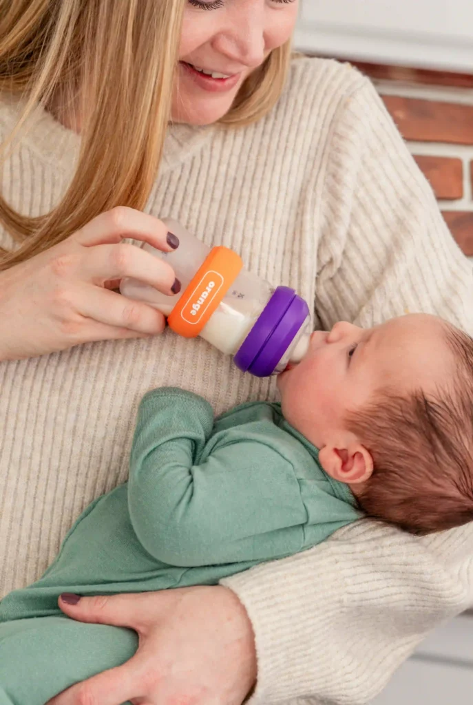 Parent feeding a newborn from a bottle fitted with an orange and purple HoopDee Hoop tracking band