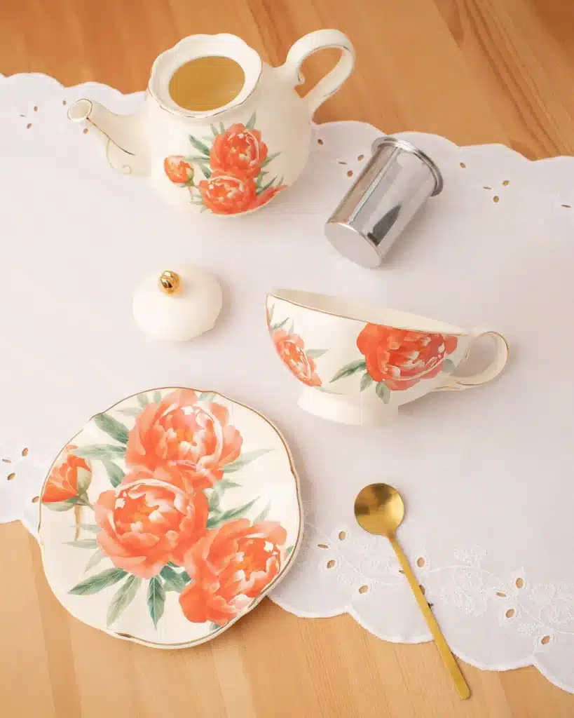 Peaceful Pursuits Peony Teaware Set flat-lay: floral teapot, cup, saucer, loose-leaf infuser, and gold spoon