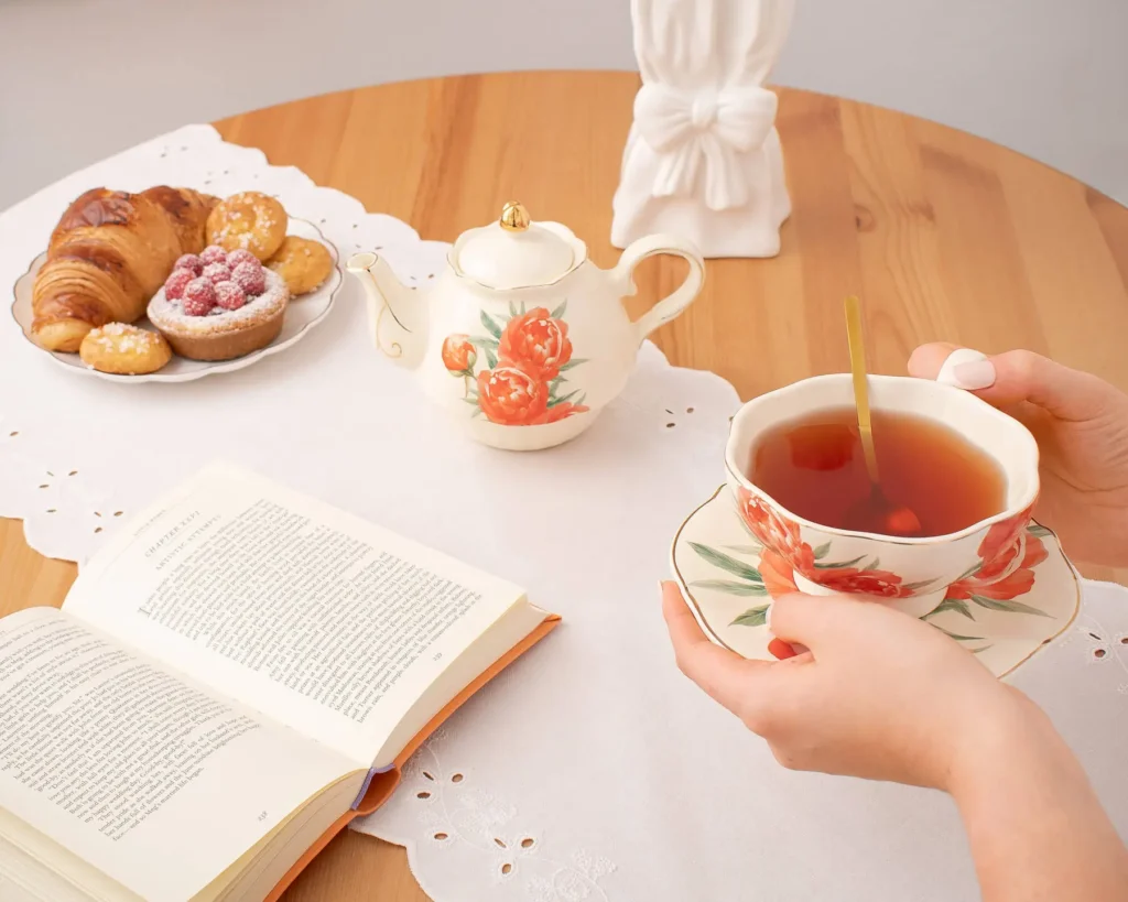 Person enjoying solo tea time with the Peaceful Pursuits peony cup and teapot beside an open book