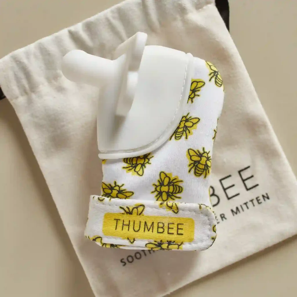 Close-up of the ThumBee pacifier mitten resting on its branded canvas pouch